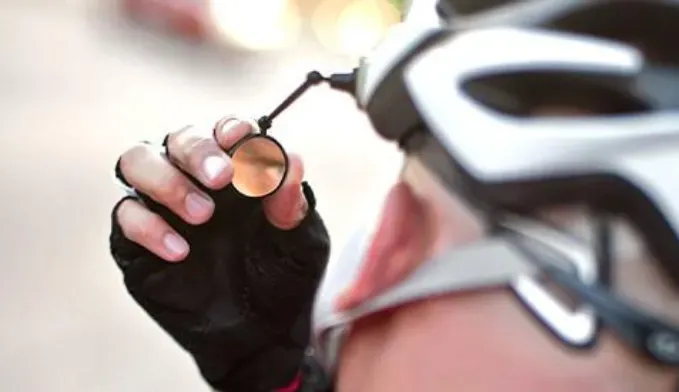 Cyclist adjusting a mirror attached to a bicycle helmet